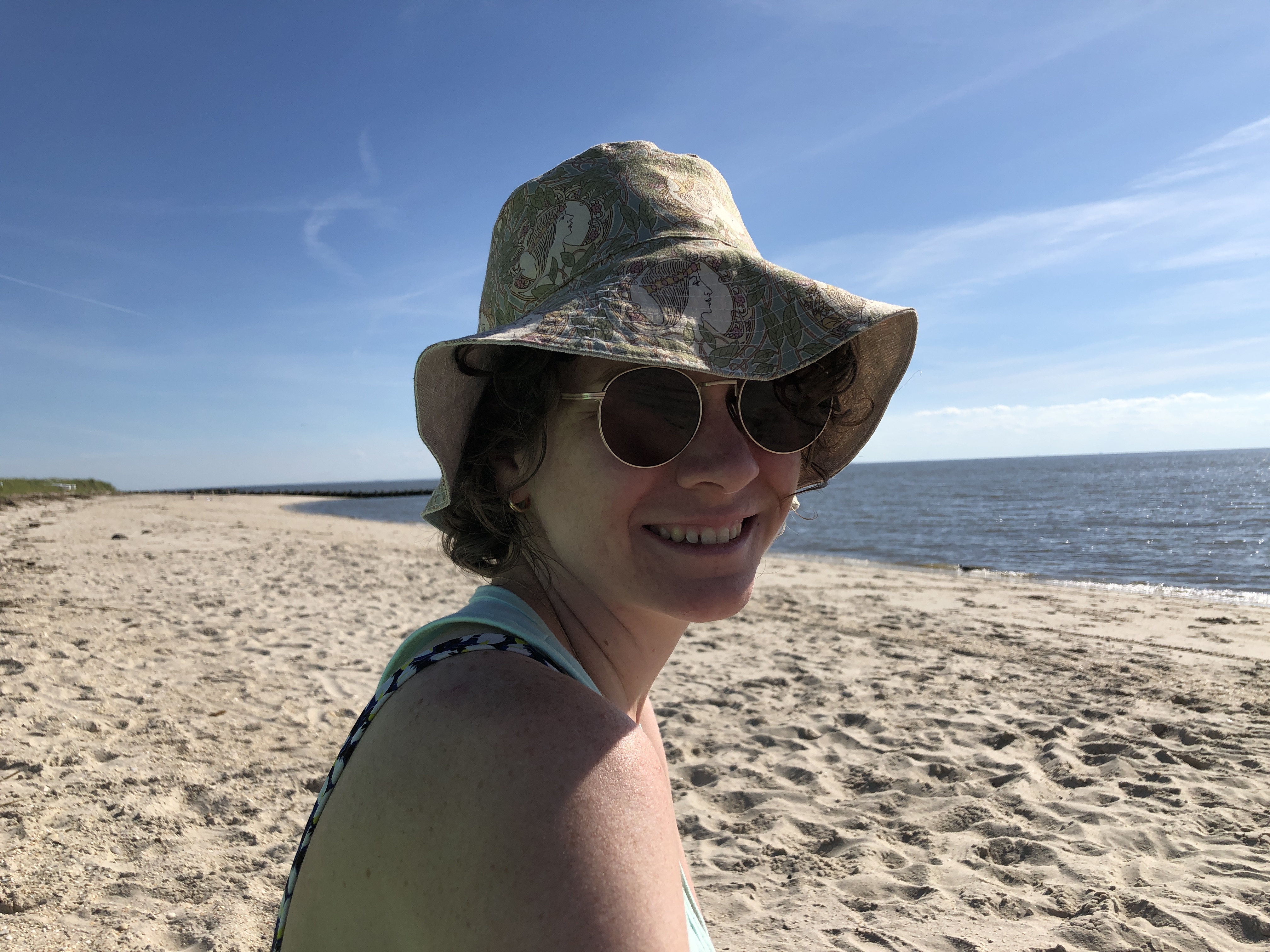 a woman at the beach wearing sunglasses and a patterned bucket hat.