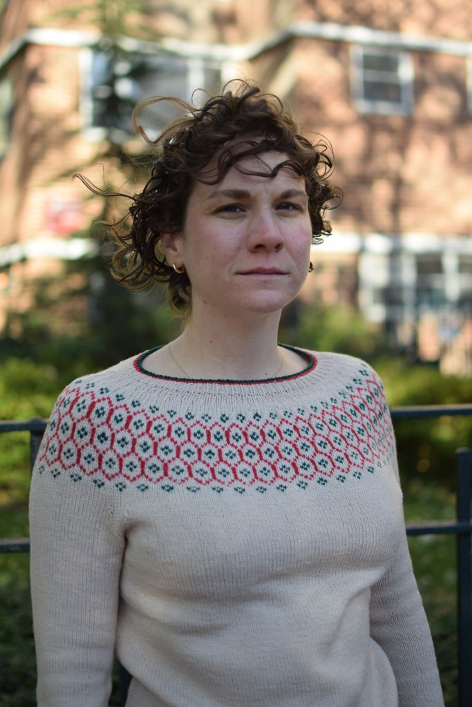 a woman stands in the city, wearing a hand-knitted sweater.