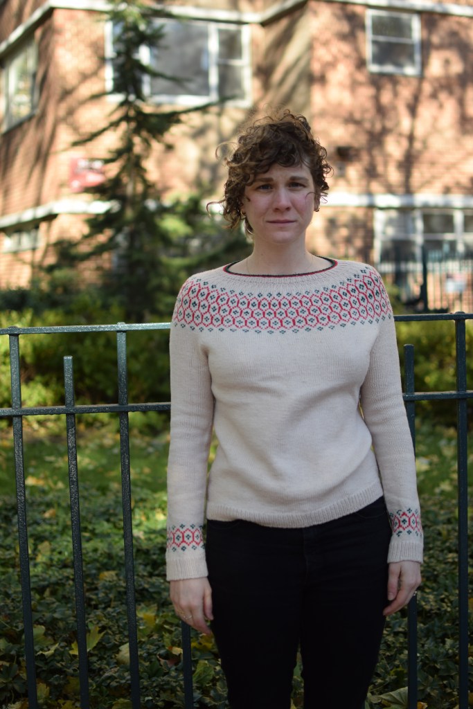 a woman stands in the city, wearing a hand-knitted sweater.