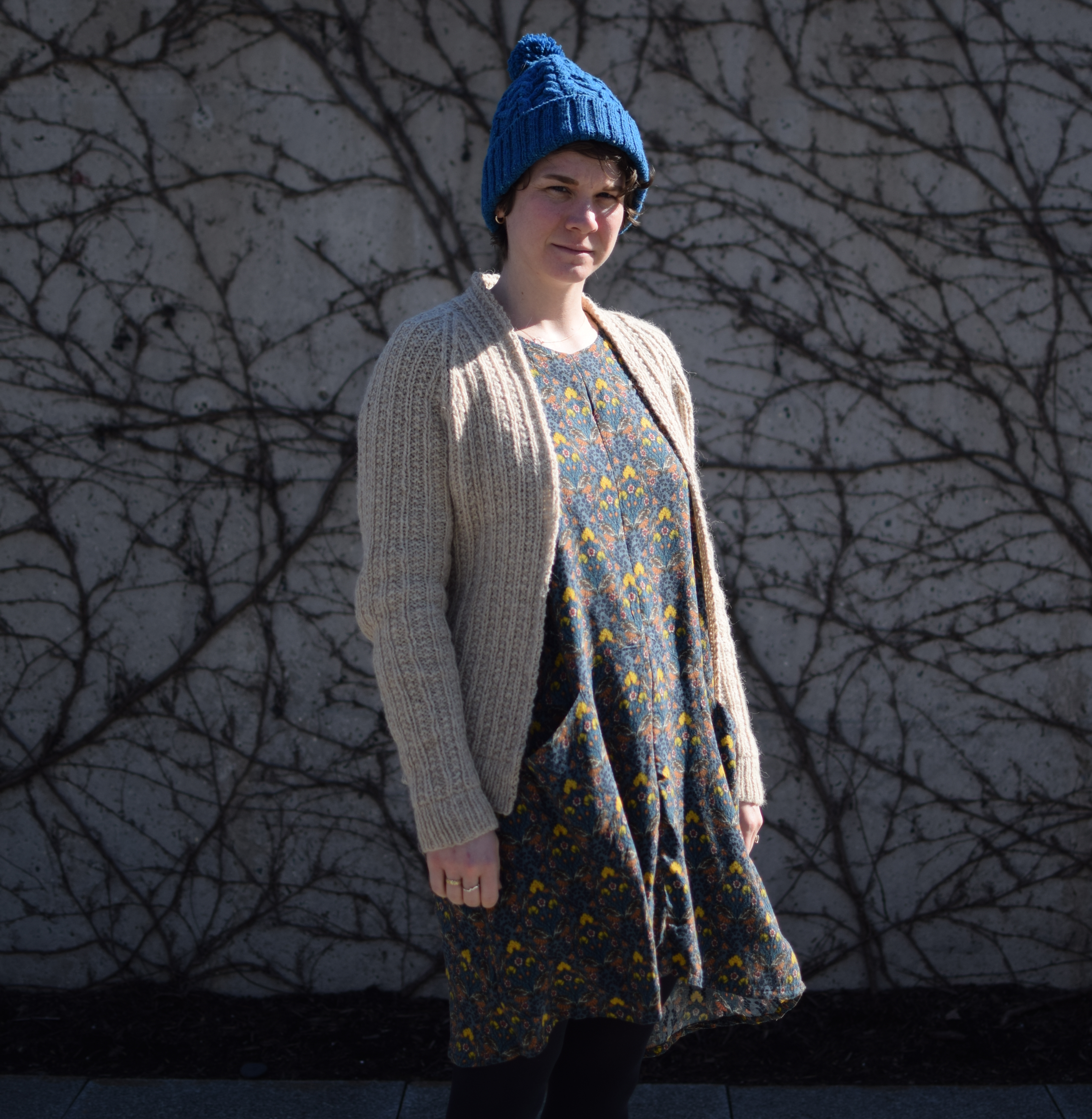 a woman stands in front of an ivy-covered wall in winter.