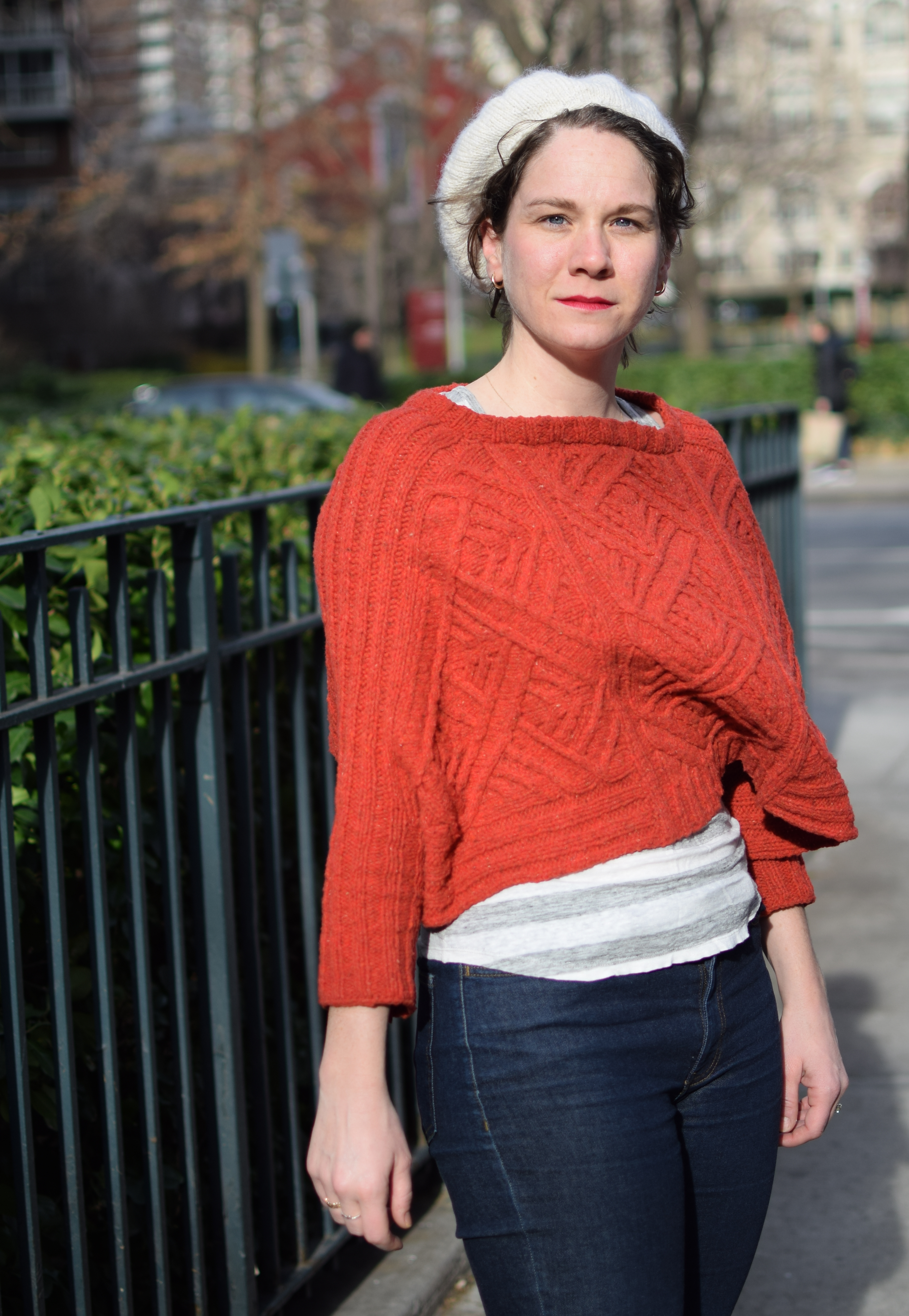 a woman poses on a windy day in a red sweater.