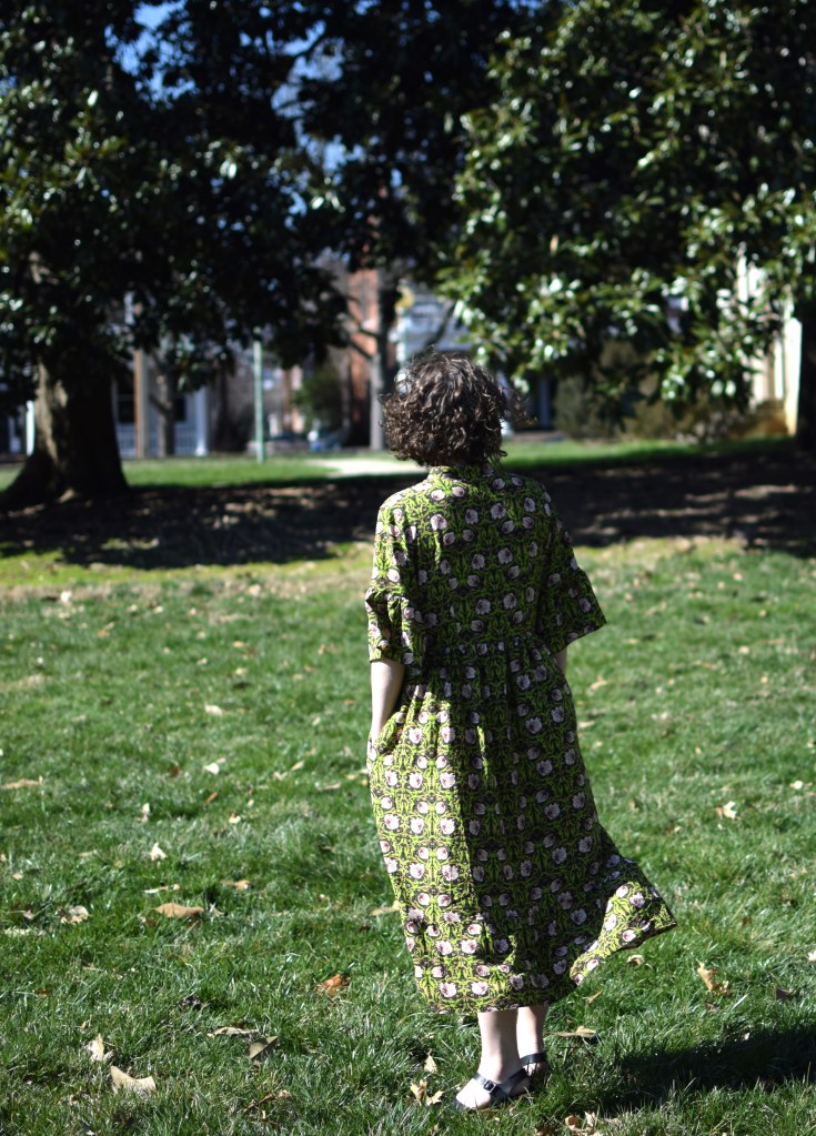 a girl wearing a green and pink floral dress in the bright sun.